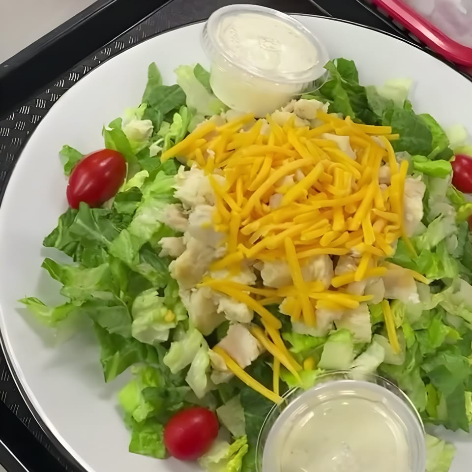 A Wrapzody salad with lettuce, shredded cheese, chicken, cherry tomatoes, and two cups of dressing.