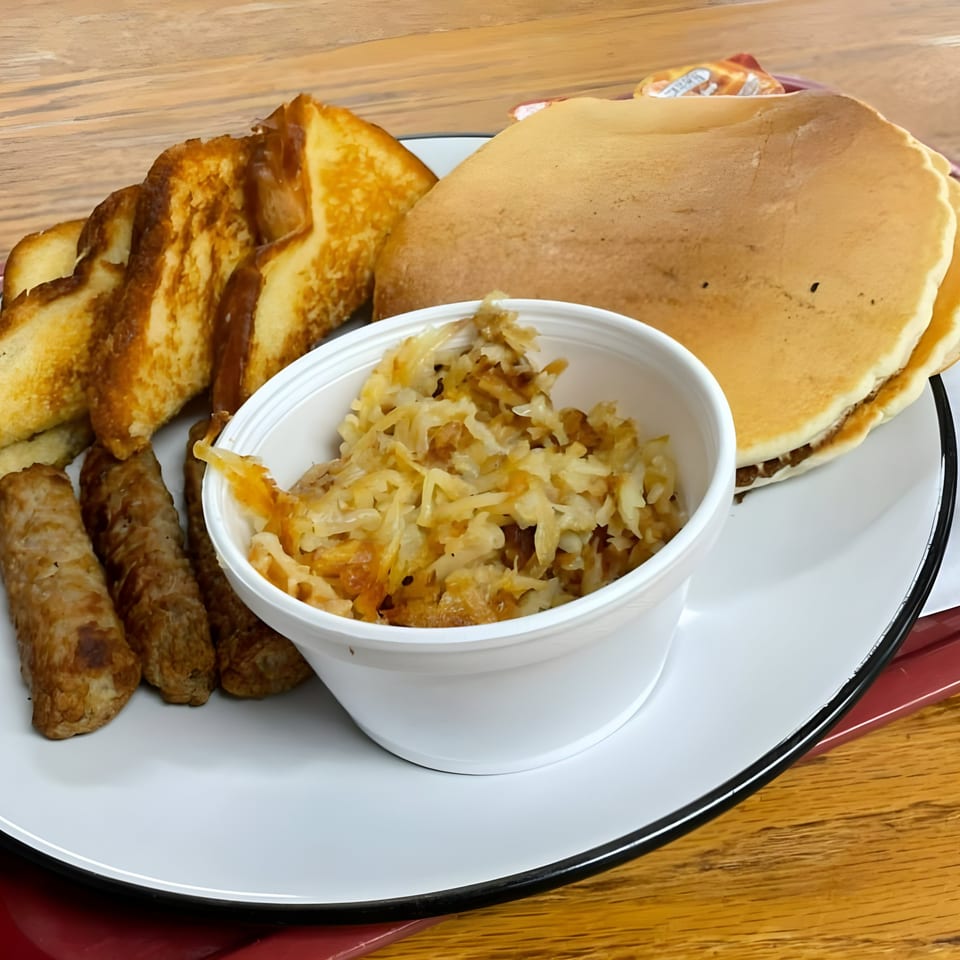 A breakfast platter with pancakes, French toast, sausage links, and a cup of hash browns.