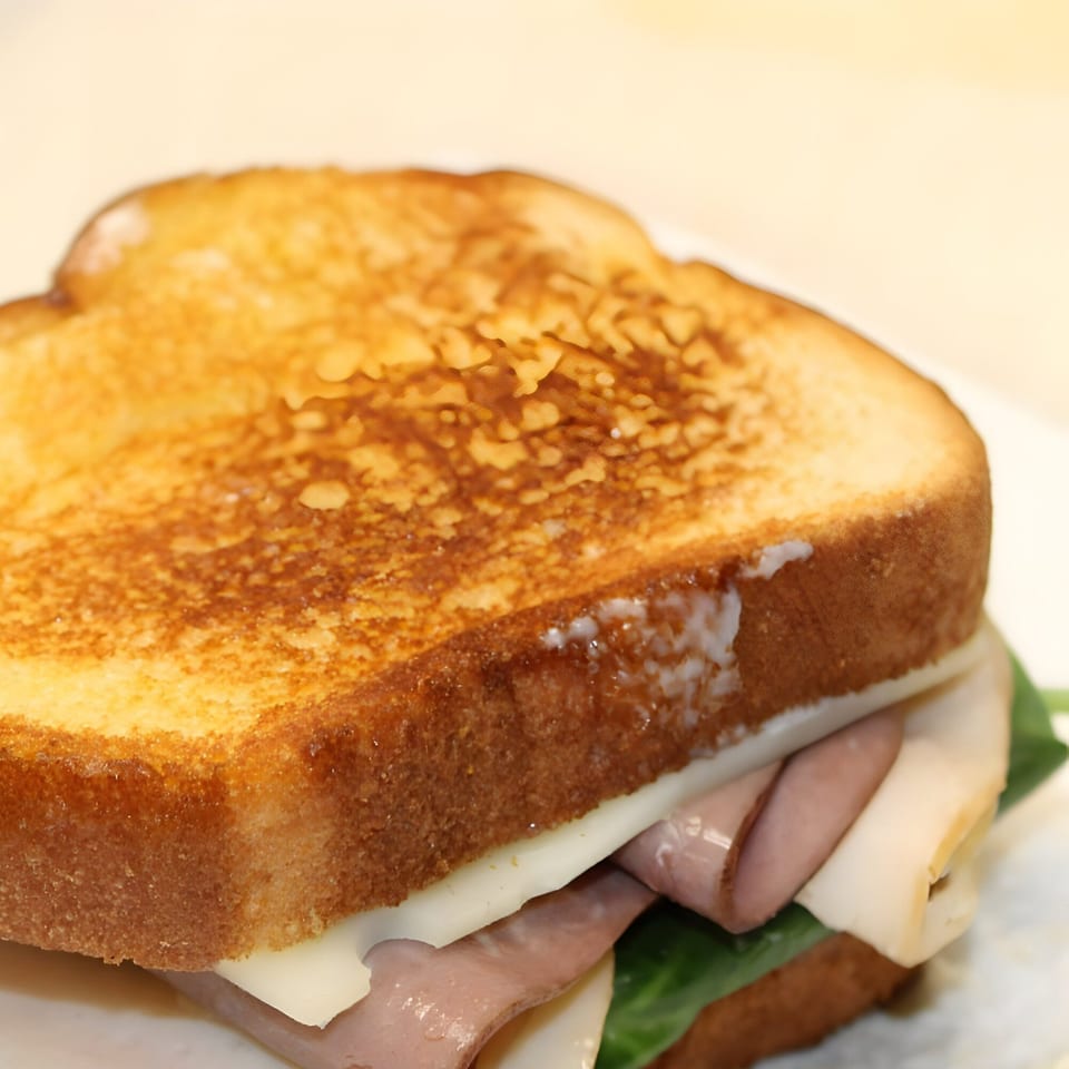 Close-up of a grilled sandwich with toasted bread, deli meat, cheese, and greens.