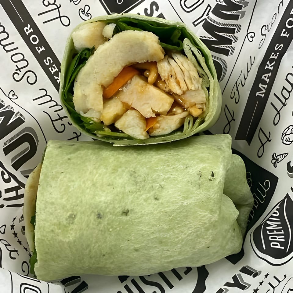 Two Wrapzody wraps on branded paper, one cut open revealing chicken, lettuce, and sauce.