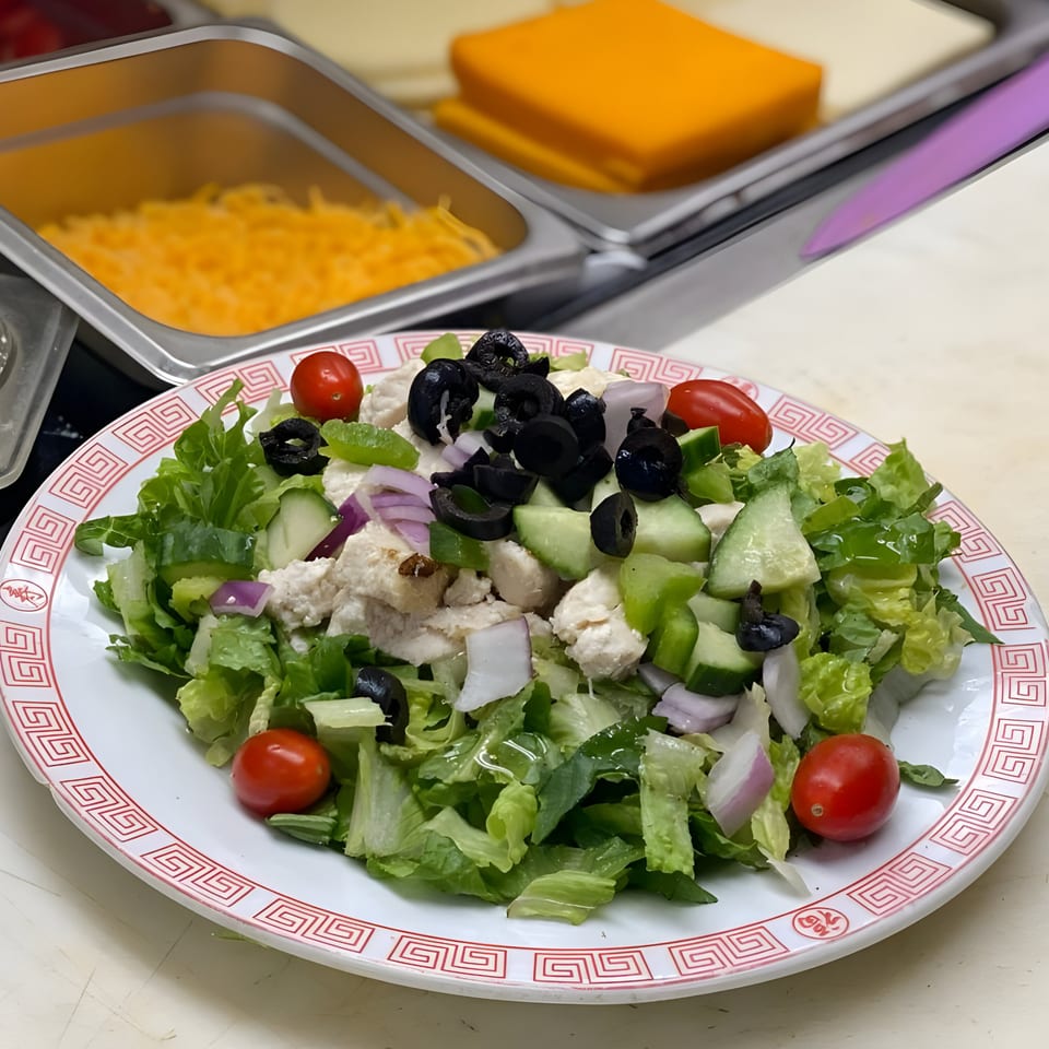 Fresh salad with lettuce, cucumbers, olives, tomatoes, and feta cheese on a white plate.