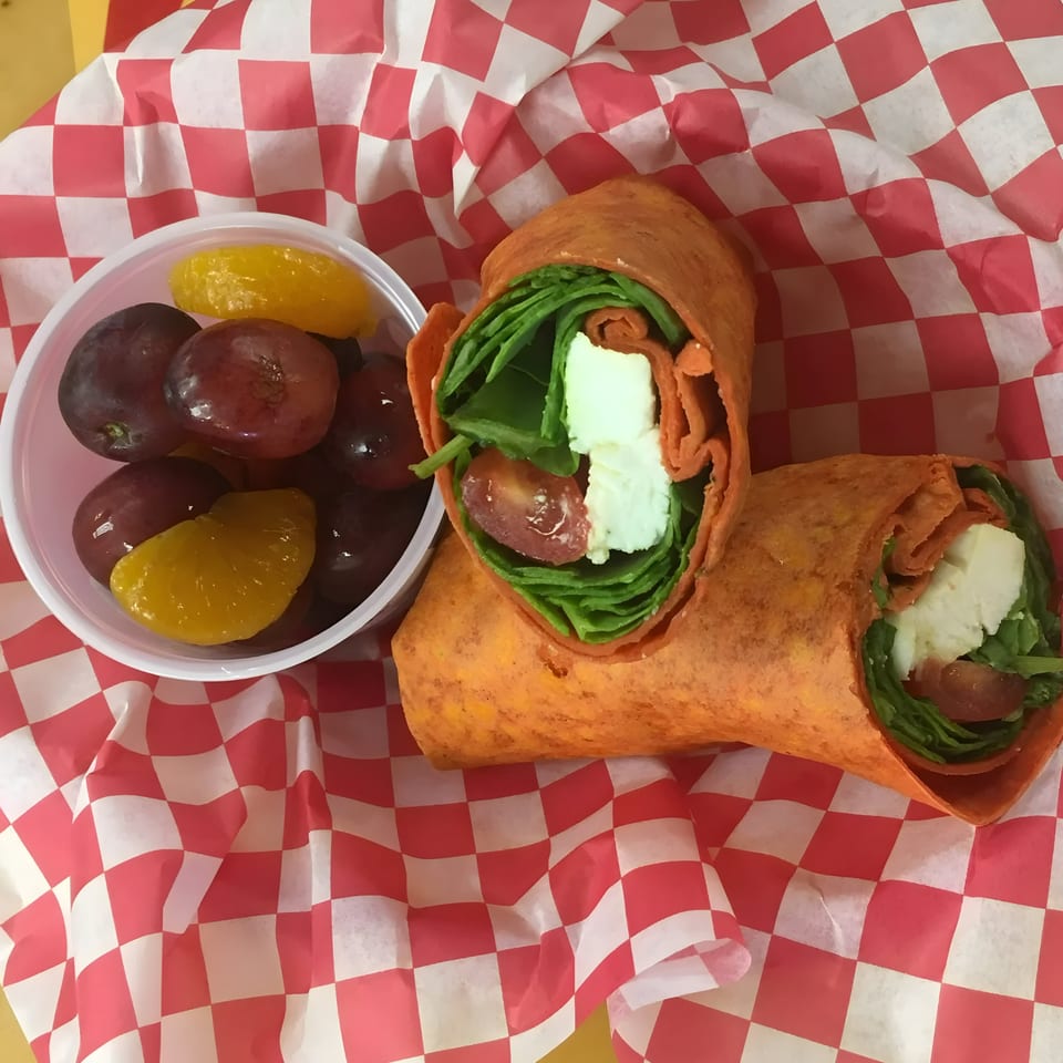 Two Wrapzody wraps with feta, spinach, and tomato, alongside a fruit cup of grapes and oranges.