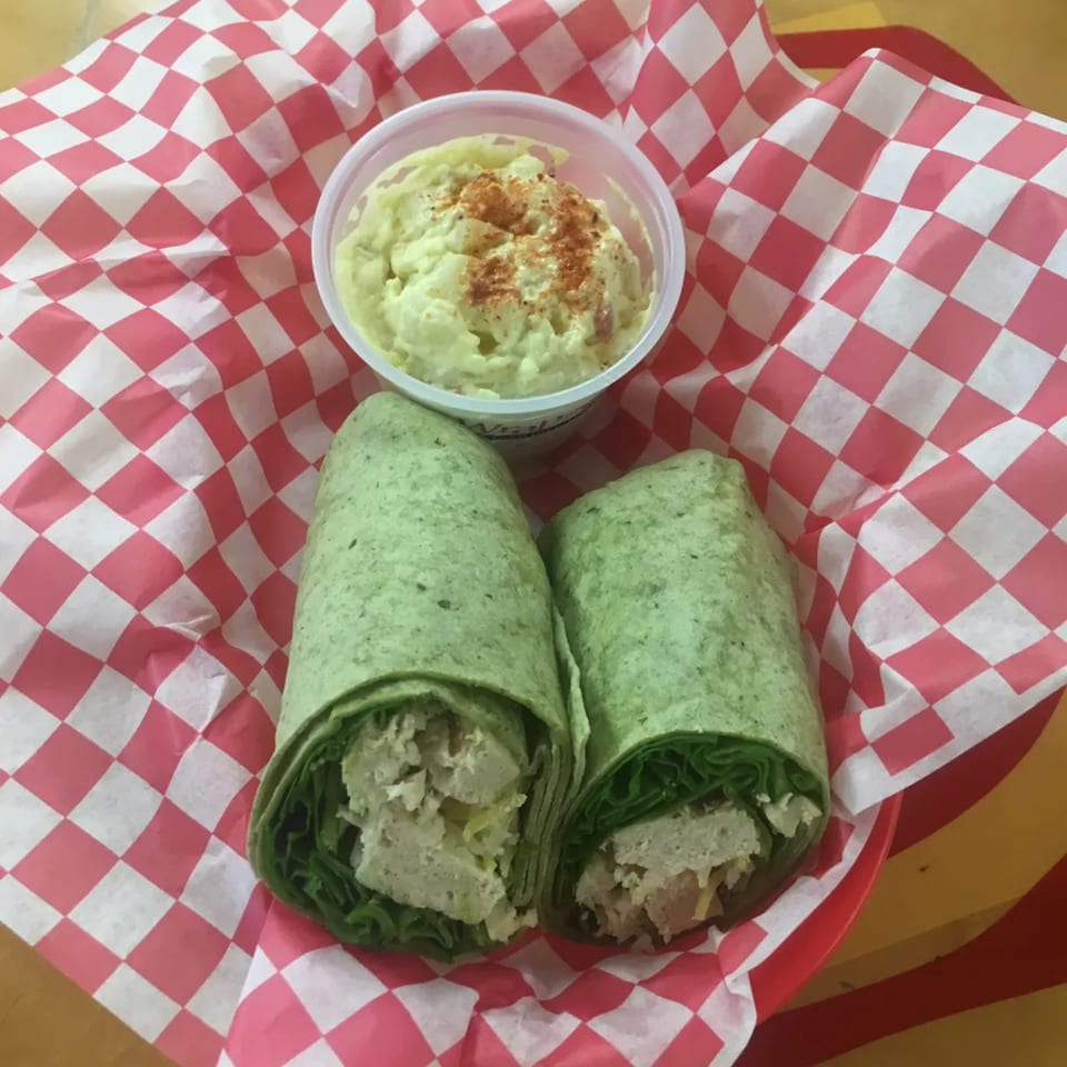 Two green wraps with chicken salad and lettuce, served with a side of potato salad.